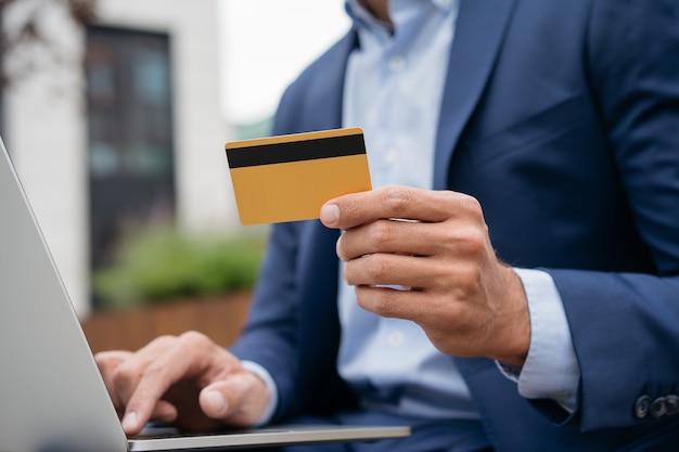 Close up of businessman hand holding golden credit card shopping online making a reservation