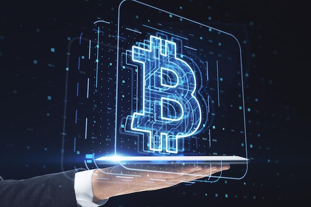 Close up of businessman hand holding tablet with glowing bitcoin hologram on blurry dark tech background Mining and trade bitcoin concept Bitcoin hits new record