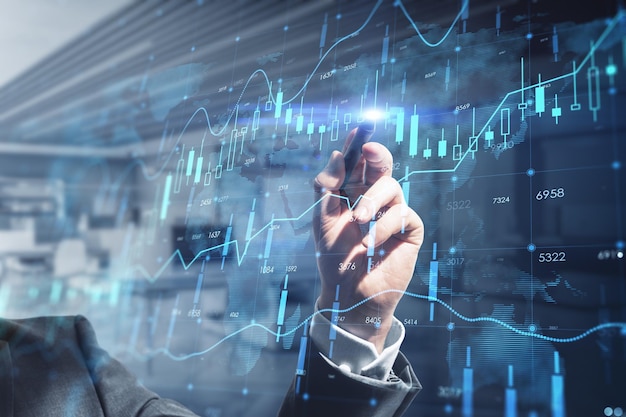 Close up of businessman hand with pen pointing at creative glowing forex chart hologram with map on blurry office interior background Stock market and invest concept Double exposure