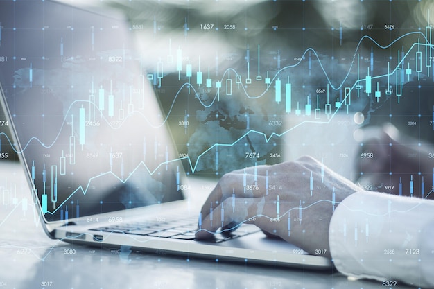 Close up of businessman hands using laptop on desktop with coffee cup and creative glowing forex chart hologram and map on blurry background Stock market and invest concept Double exposure