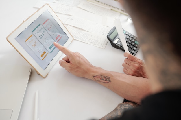 Photo close-up of businessman sitting at the table and working on digital tablet with financial report on the screen at office