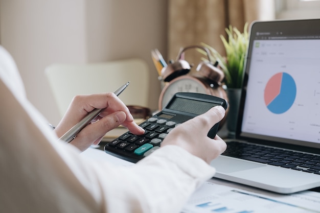 Close up of businesswoman or accountant hand holding pen working on calculator