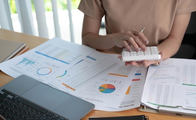 Close up of businesswoman or accountant using calculator to calculate calculate business data working at office with paper document and laptop computer on office table business and finance concept