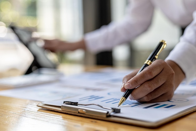 Close-up businesswoman's hand holding a pen pointing at a bar chart on a corporate financial information sheet, the businesswoman examines the financial information provided by the finance department.