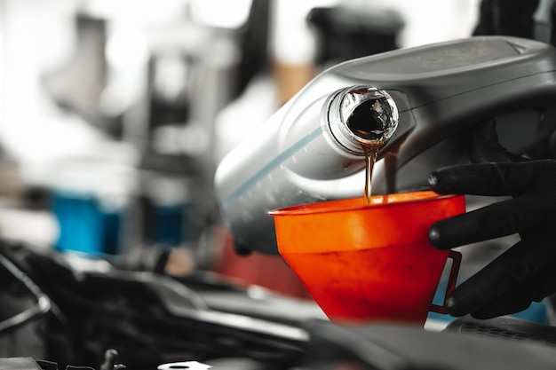 Close up of car service worker pouring new oil into car engine