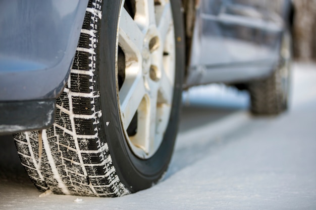 Close up of a car tire parked on snowy road on winter day. Transportation and safety concept.