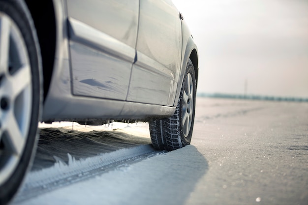 Close up of a car tire parked on snowy road on winter day. Transportation and safety .