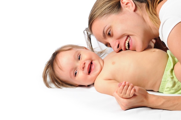 Close-up a caring young mother play with a little cute half-year-old girl after bathing on a white