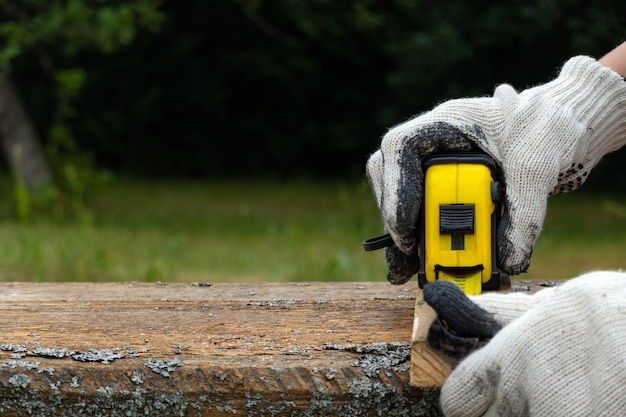 Close up of carpenter hand wearing working gloves and measuring plank with a tape measure.