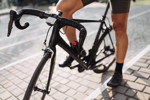 Close up of caucasian cyclist in activewear and sneakers standing on city street with black bike Sporty man taking break during outdoors training