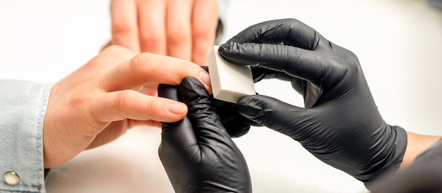 Close up of the caucasian hands of a professional manicurist are filing the nails of a young woman Young caucasian woman receiving a manicure by a beautician with a nail file in a nail salon