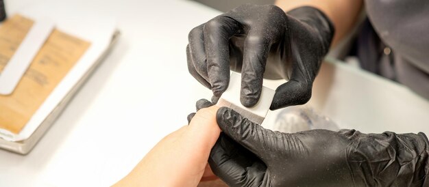 Close up of the caucasian hands of a professional manicurist are filing the nails of a young woman Young caucasian woman receiving a manicure by a beautician with a nail file in a nail salon