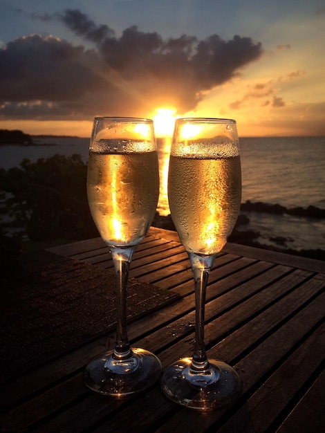 Close-up of champagne flutes on table against sea during sunset