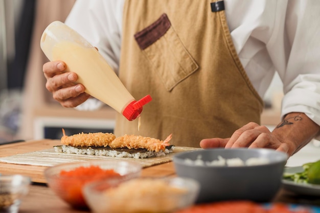 Close up chefs male hands squeezes the sauce on sushi sushi roll food delivery