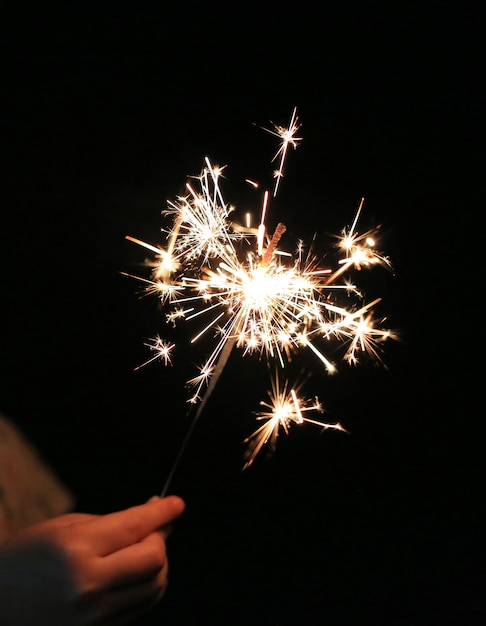 Close-up child hand holding fire sparklers on the dark at festival.