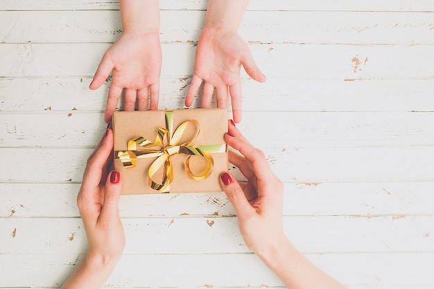 Close up of child and mother hands with gift box over wood background.