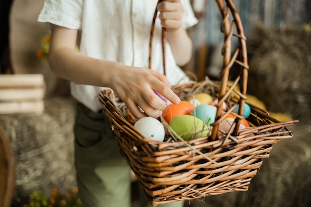 Close-up of a child's hand picking out colorful eggs in a wicker basket. Easter Holiday