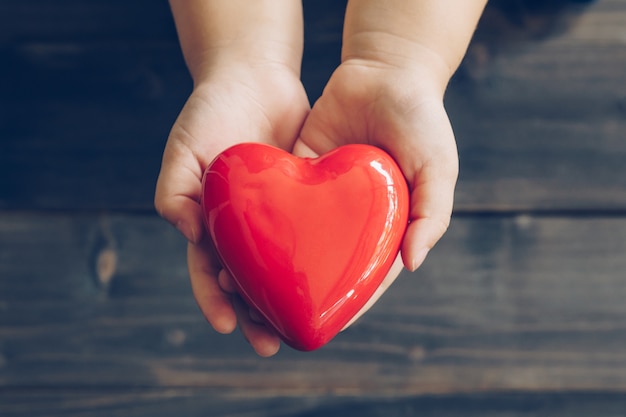 Close up children hands giving red heart on wood background