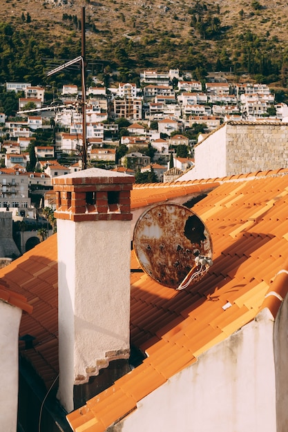 Close-up of a chimney and dish antennas on the orange roof tiles of a house