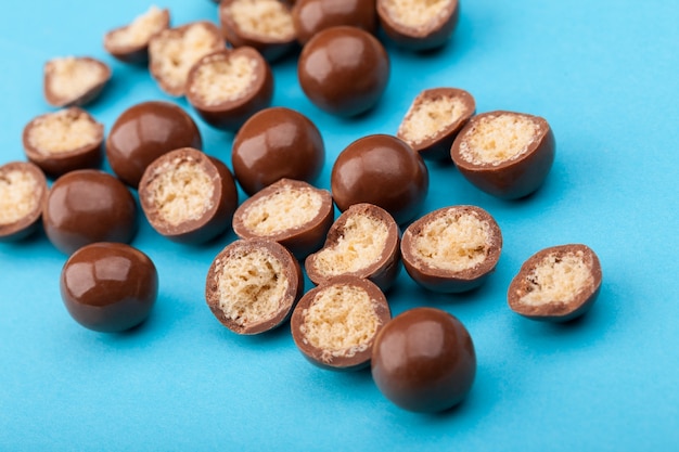 Close up of chocolate candy balls and halves with crispy corn filling on blue background