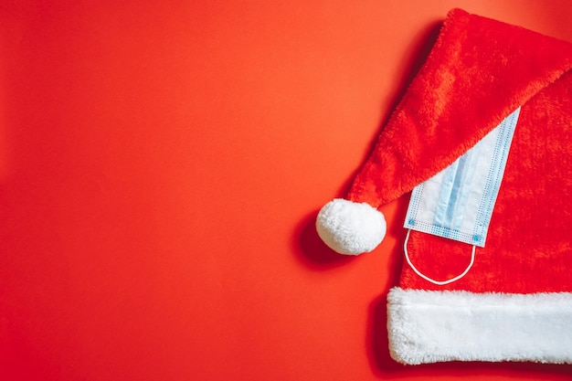 Close-up of Christmas santa hat and medical mask on a red background. New year and pandemic concept.