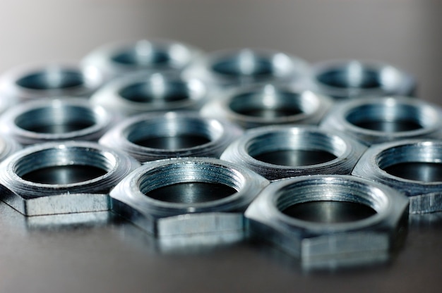 Close-up chrome metal nuts in the form of honeycombs lie next to each other forming an area. Background concept for fasteners and construction topics. Repair and spare parts concept