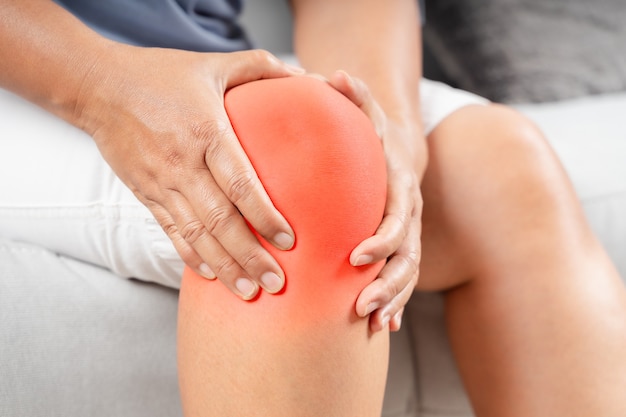 Close up of chubby woman sitting on the sofa and feeling knee pain and she massages knee.