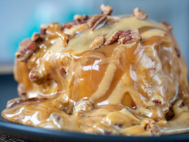 Close-up of a cinnamon bun topped with caramel topping and pecans. Black plate, side view. Delicious sweet dessert