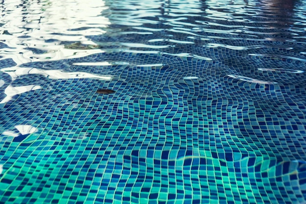 A close up of a clean swimming pool water at the light-blue tiled floor background. One swimming pool drain under rippling indoor pool water. A shallow swimming pool with beautiful water blinks.