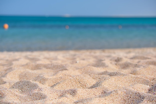 Close up of clean yellow sand surface covering seaside beach with blue sea water on background. Travel and vacations concept.