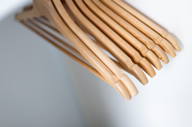 Close up of cloth  wooden hangers in row on white wall. Hangers in wardrobe.