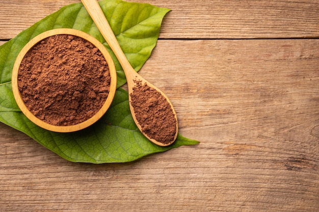 Close up Cocoa powder in wooden bowl and green leaf on wooden table