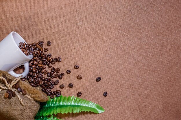 Close up coffee beans with coffee burlap bag and a white cup on old wooden background.