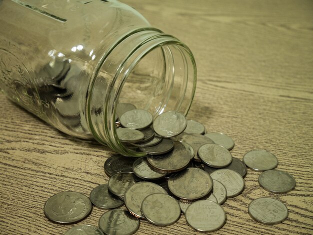 Close up coins and jar lie on wooden table