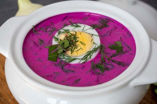 Close-up of cold chlodnik soup on a wooden board. Soup of Polish Belarusian and Russian cuisine made of beetroot and kefir, decorated with half an egg. Healthy food