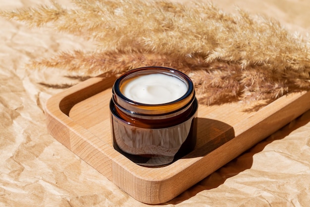 Close up of collagen cream in open glass jar and dry flowers reeds on beige background Set for skin and body care beauty products