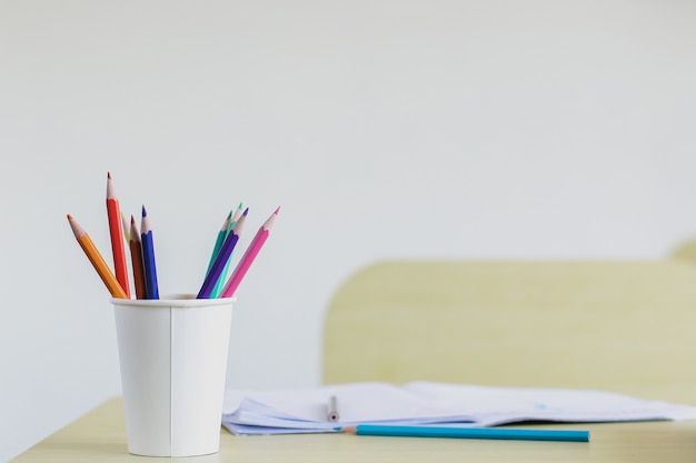 Close up of colored pencils in a Styrofoam cup on wooden desk