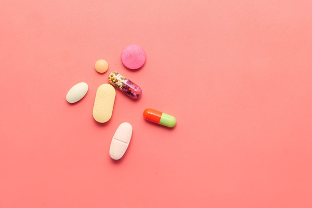 Close up of colorful pills and capsule on pink background .