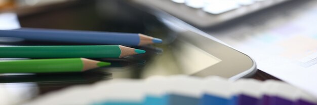 Close-up of colourful pencils on modern device. Macro shot of office details. Company supplies for work. Black screen of gadget. Technology and business growth concept