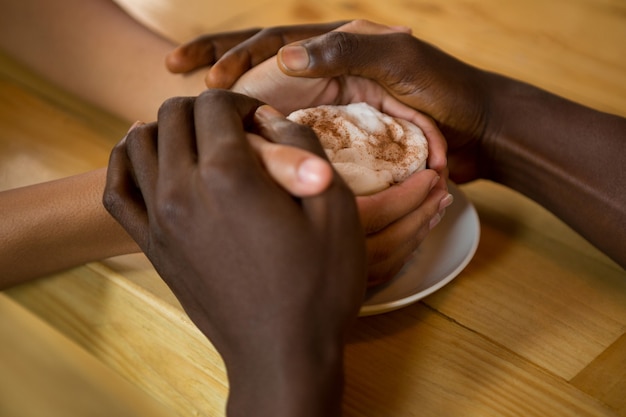 Close-up of couple holding hands and coffee cup in coffee shop