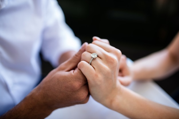 Close-up of couple holding hands with engagement ring