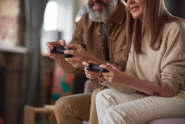 Close-up of couple using joysticks and playing online video games on the sofa in the room