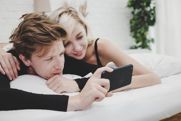 Photo close-up of couple watching video on mobile phone while lying on bed