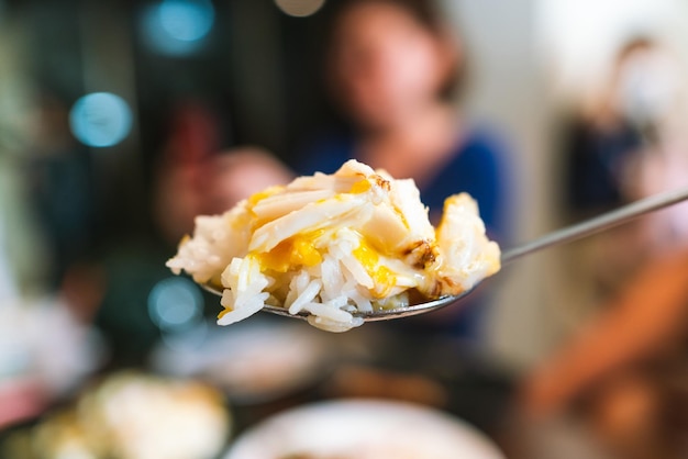 Close up crab omelette over rice in a spoon The fluffy omelette with chunks of fresh crab meat is placed on a mound of steamed rice and topped with sliced scallion Chineseinfluenced menu in Bangkok