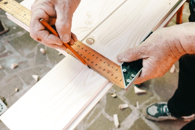 Close-up of craftsman hands in measuring wooden plank with angular ruler and pencil. Woodwork concept.