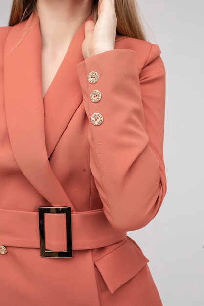 Close-up crop stock photo of an anonymous model wearing coral jacket with beige buttons and belt with metallic buckle. Studio shot. Online shop concept.