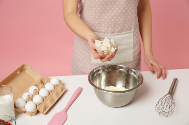 Close up cropped female chef cook confectioner or baker in apron white t-shirt cooking cake or cupcake table hold butter isolated on pink pastel background in studio. Mock up copy space food concept.