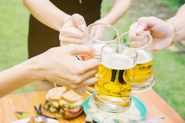 Close-up cropped image of friends clinking with beer in garden