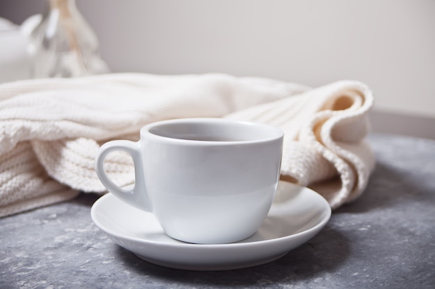 Close up of cup of coffee and knittead white plaid on the gray 