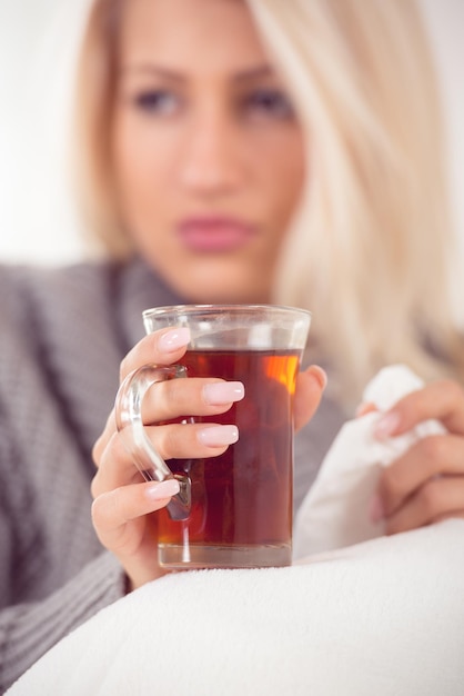 Close-up cup of tea held by the hand of girl, with a face out of focus, dressed in wool sweater,  tucked in a blanket.